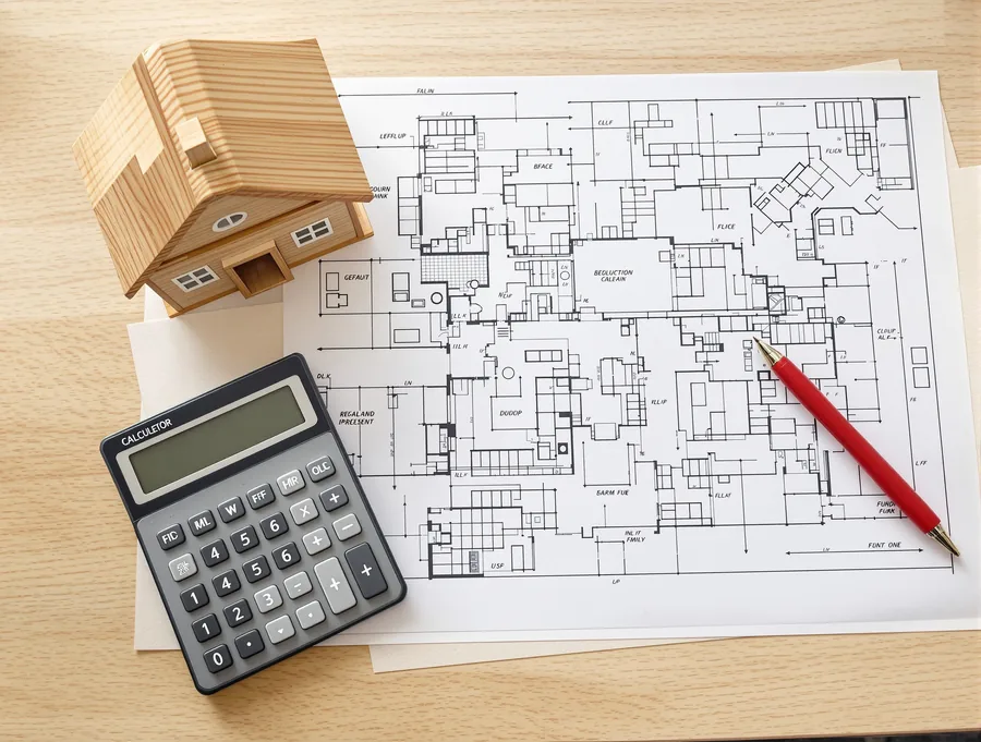 ADU building plans, a calculator and a model house on a desk