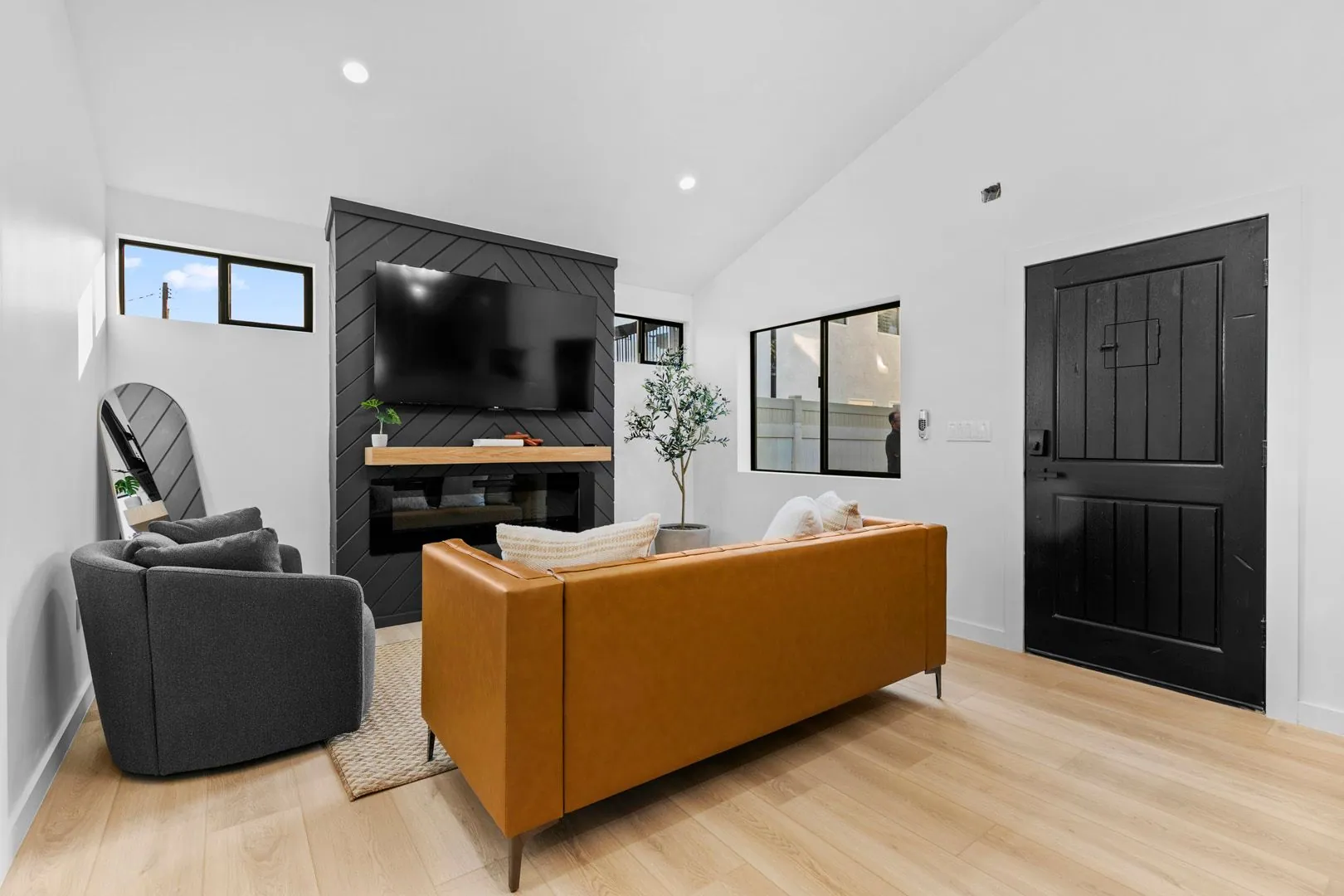 ADU living room with tan leather sofa, black shiplap accent wall and vaulted ceiling