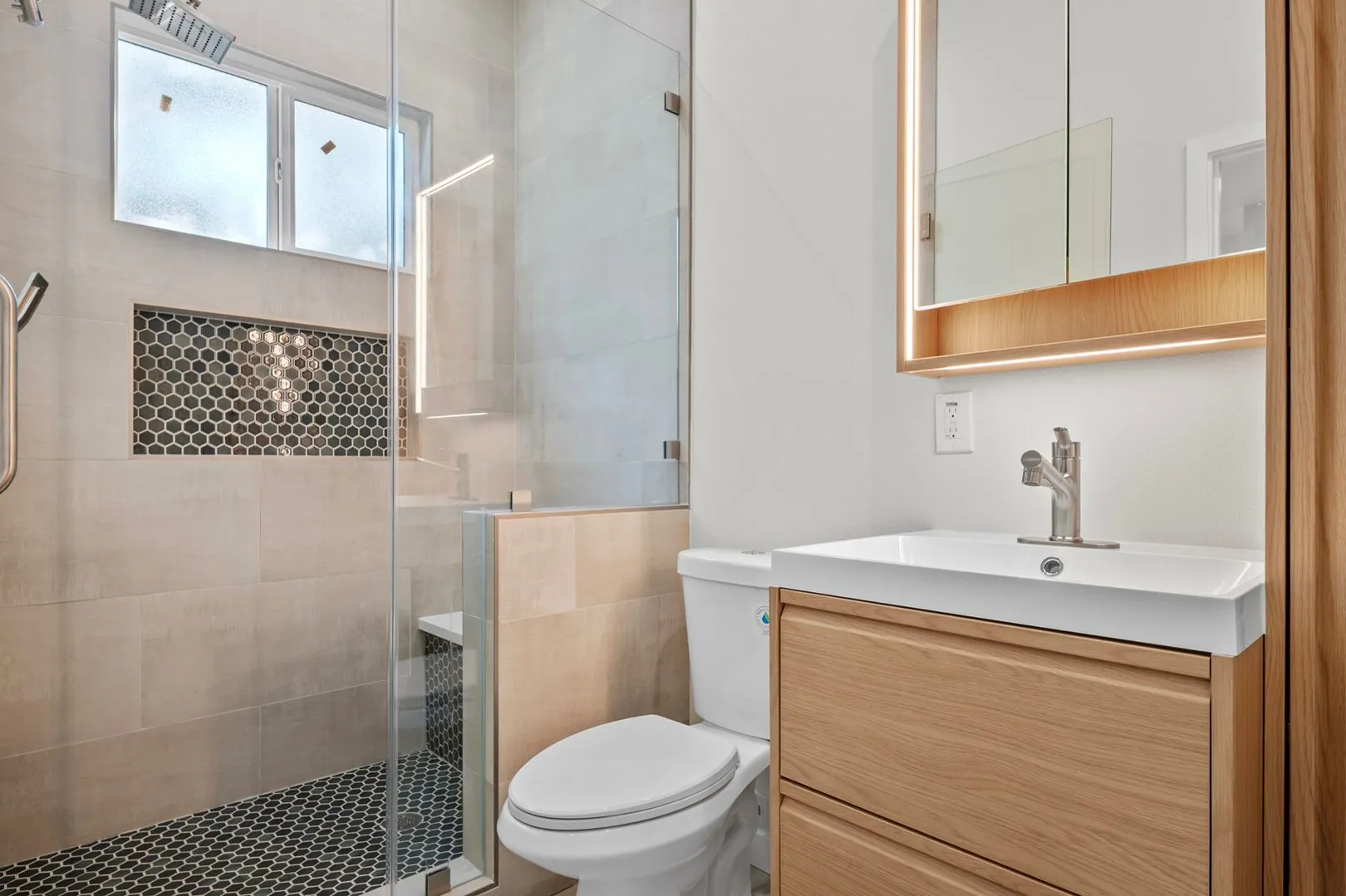 ADU bathroom with walk-in glass shower, hexagon mosaic niche, floating oak vanity and backlit mirror