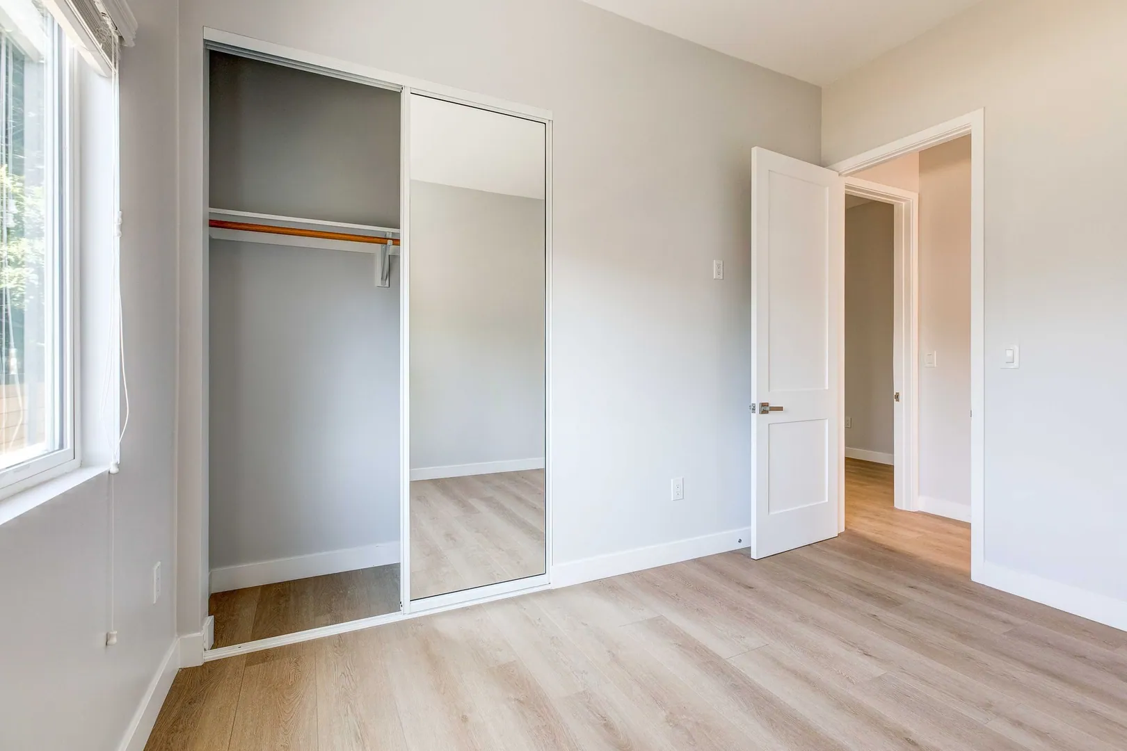 ADU bedroom with light oak floors, mirrored closet and large window